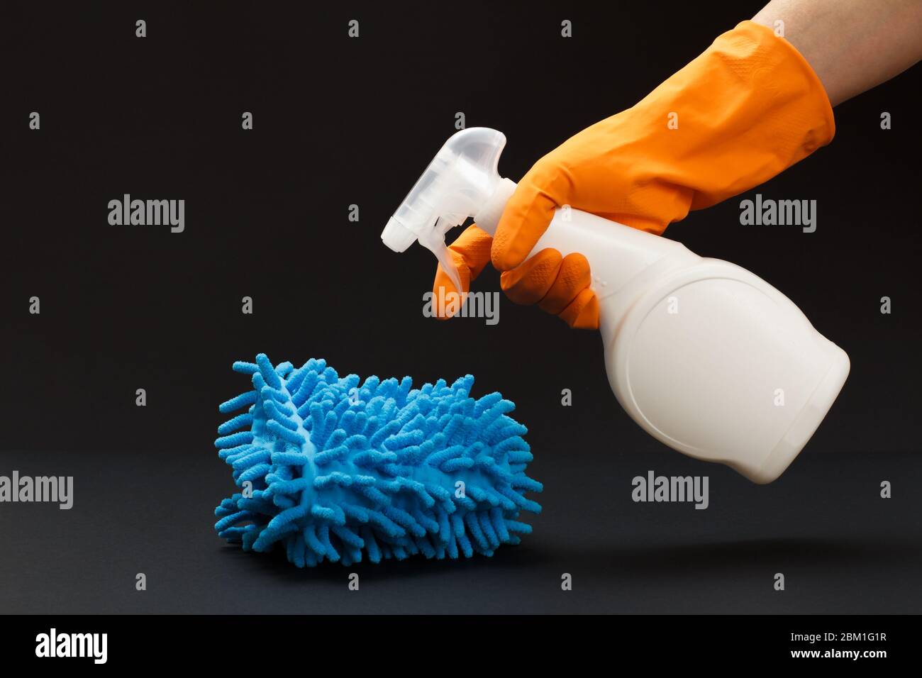 Hand in rubber glove holding a plastic bottle of washing liquid and a ...
