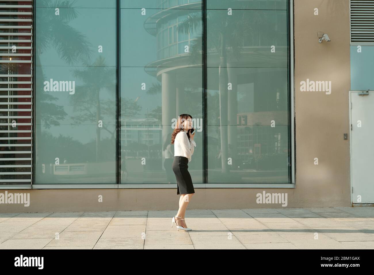Beautiful female business woman walks in city park  and talking on cell phone Stock Photo
