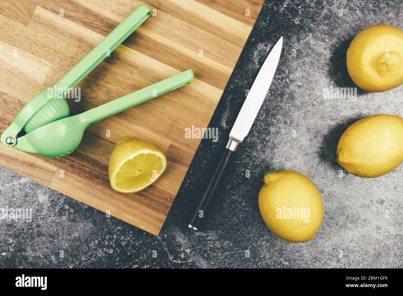 directly above view of ripe organic lemons on kitchen counter with wooden cutting board, knife and citrus juicer Stock Photo