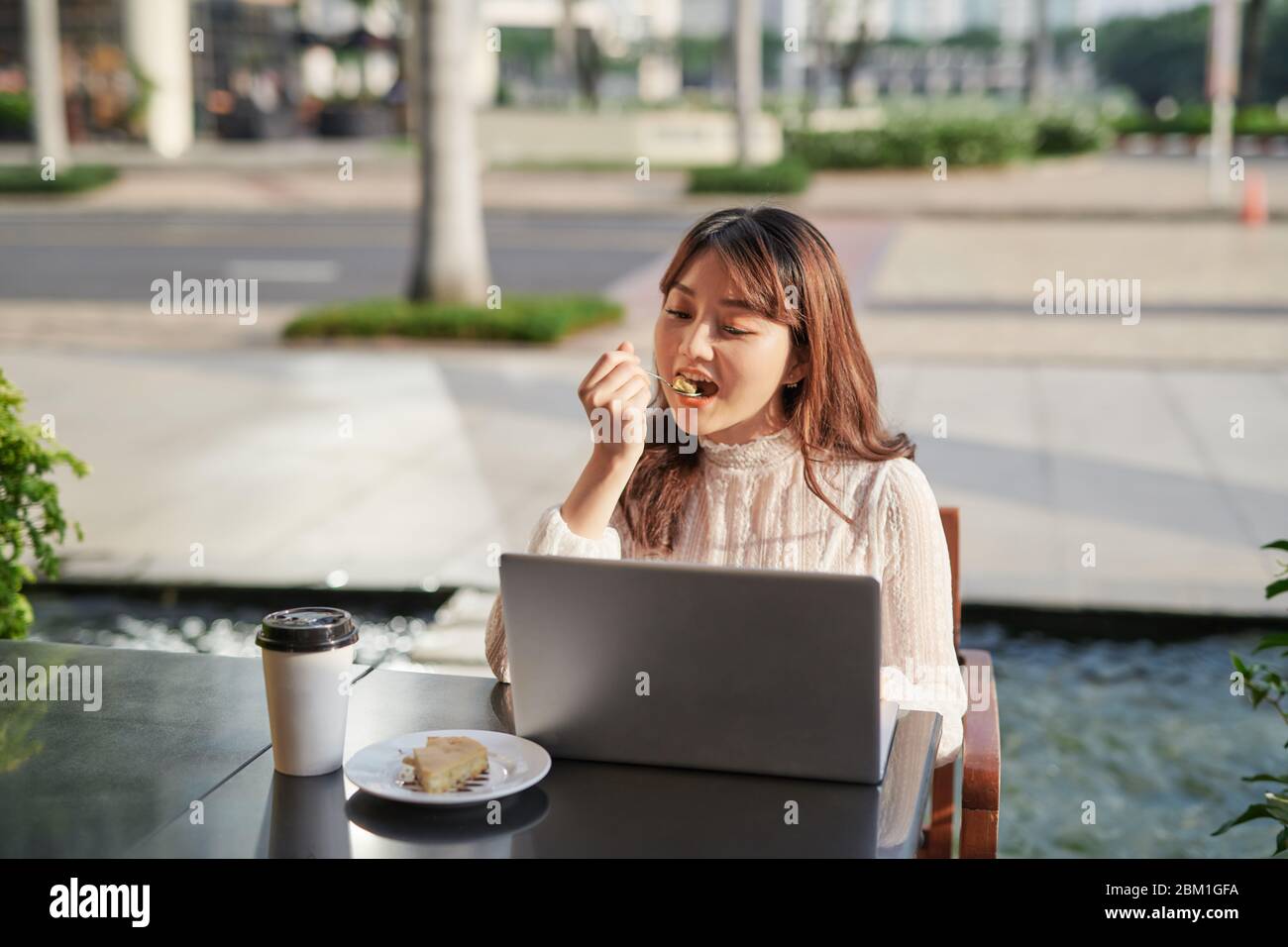 Beautiful woman eating delicious banana cake in a coffee shop. Girl in front of laptop in a coffee shop. Girl enjoying tasty cake. Stock Photo