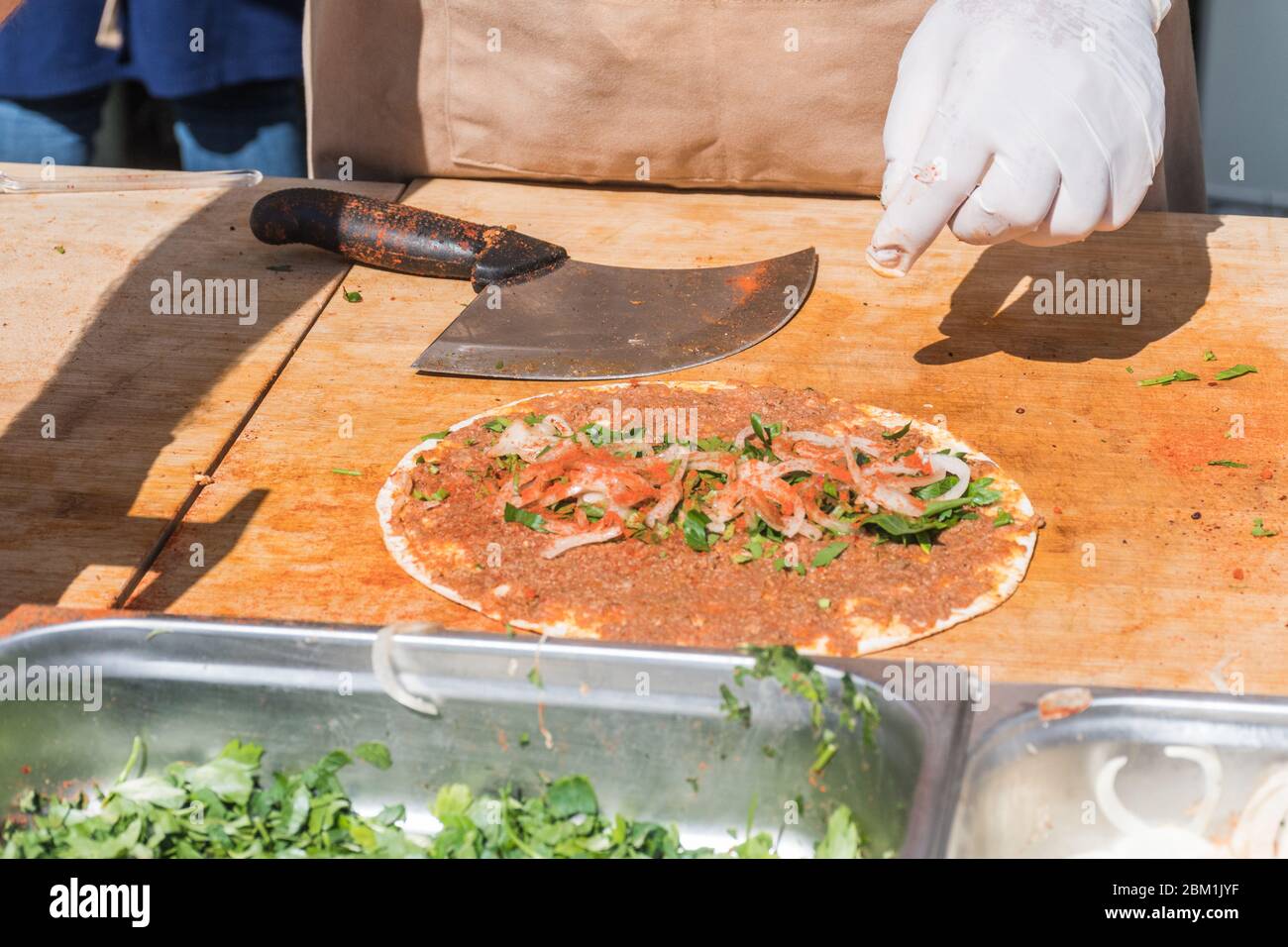 Traditional Turkish pizza, called Lahmacun, being prepared with meat, onion and parsley, displayed on a wooden table at a a street food market Stock Photo