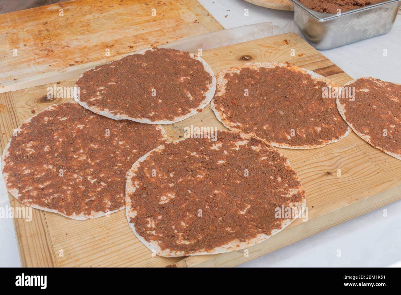 Traditional Turkish pizza, called Lahmacun, being prepared with meat, onion and parsley, displayed on a wooden table at a a street food market Stock Photo