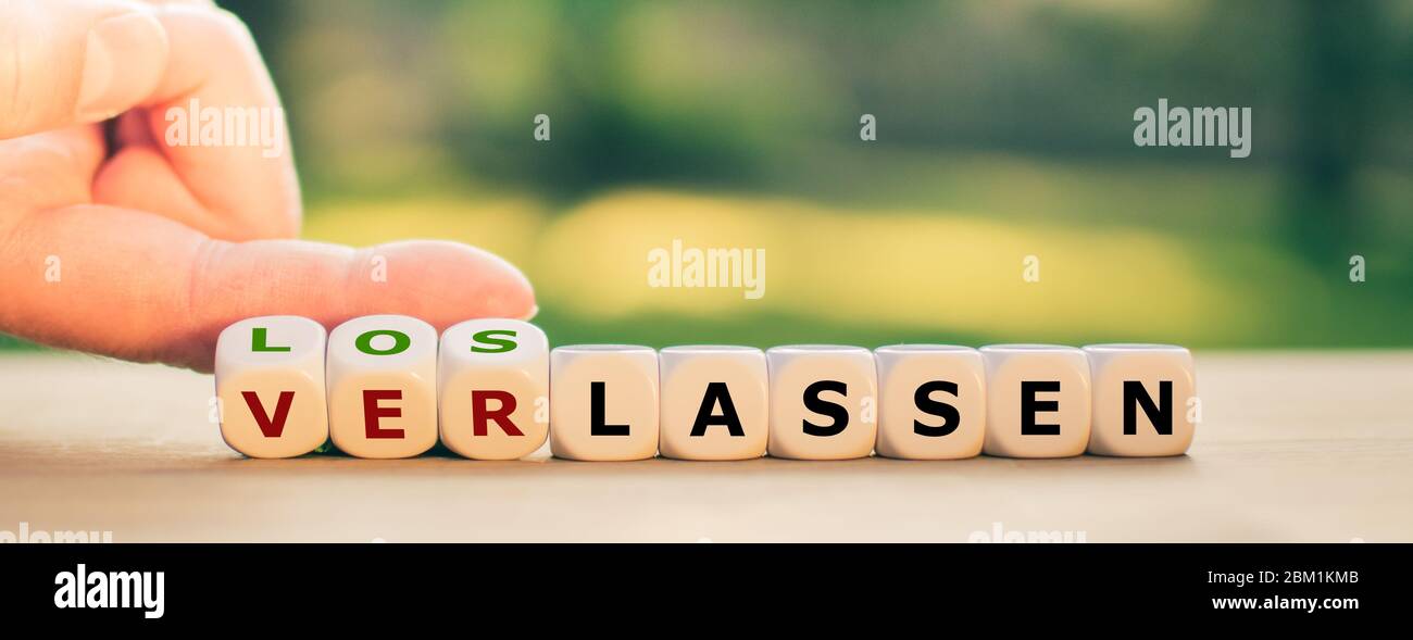 Hand turns dice and changes the German word 'verlassen' ('to leave someone') to 'loslassen' ('to let go'). Stock Photo