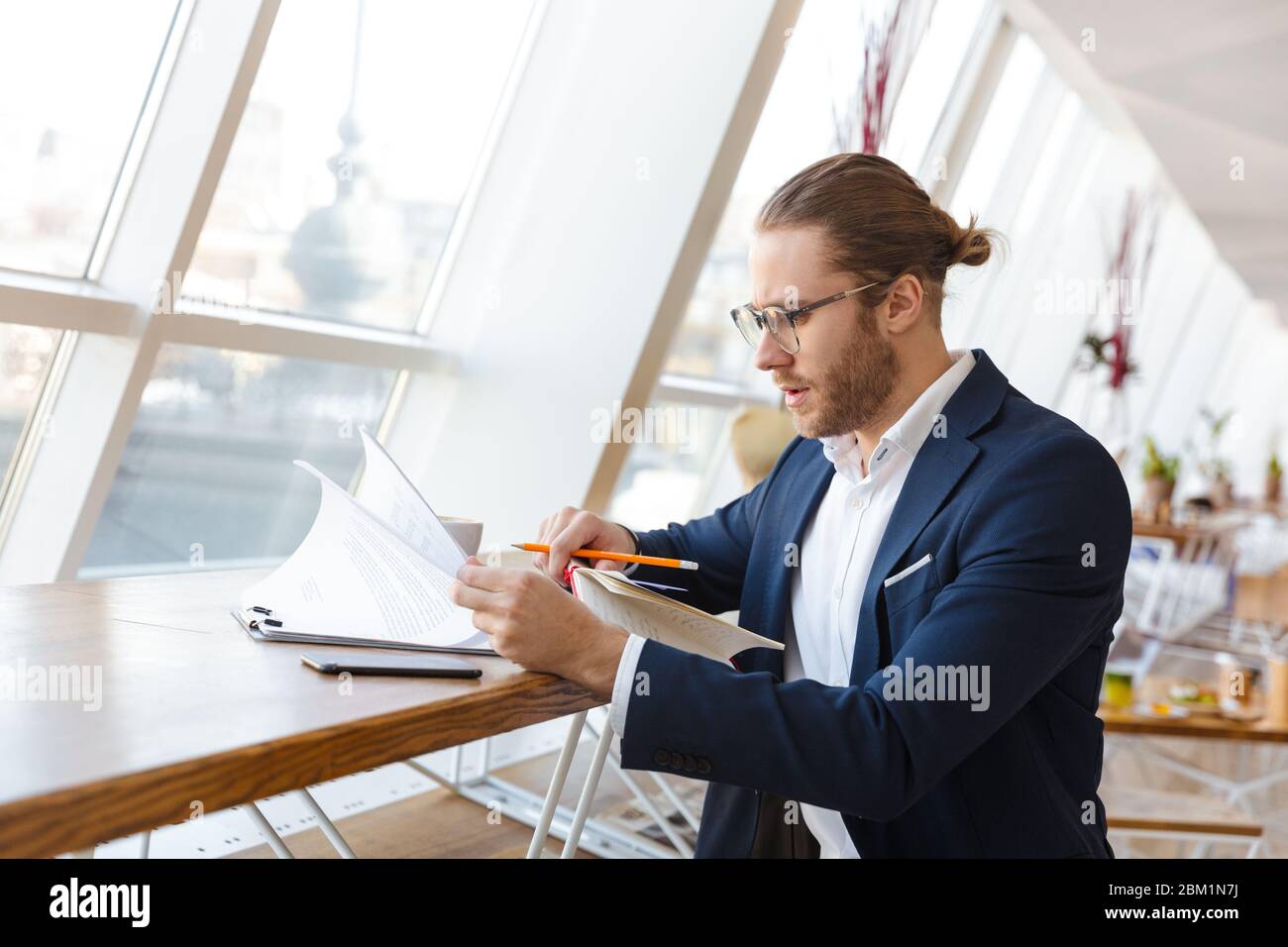 Image of concentrated handsome young businessman indoors in office work with paper documents. Stock Photo