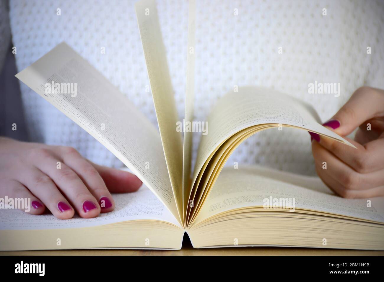 A young woman with a neat pink manicure sitting at table and browses in a book Stock Photo