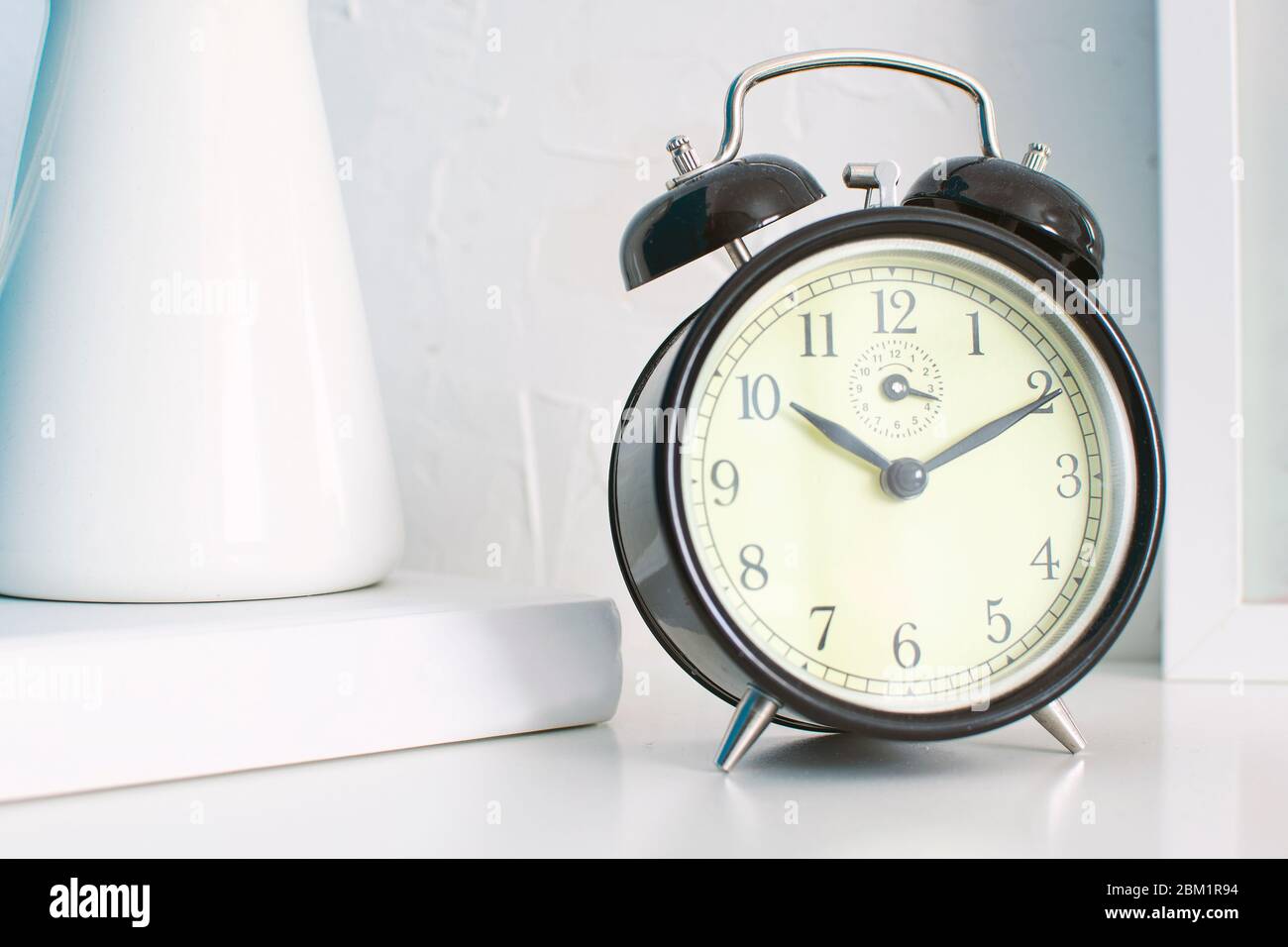 Close up of alarm clock on a bedroom. White wooden bedside table and empty copy space for Editor's text. Stock Photo