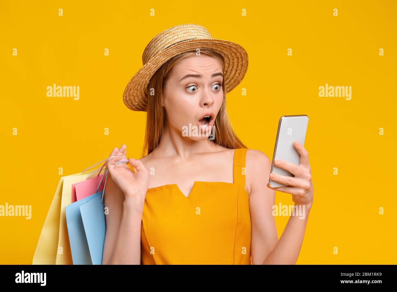Big Summer Sales. Shocked Millennial Girl Holding Smartphone And Shopping Bags Stock Photo