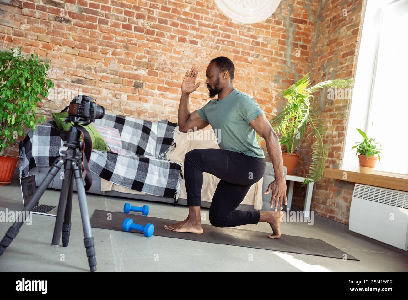 African-american man teaching at home online courses of fitness, aerobic, sporty lifestyle while being quarantine. Activity during insulation, wellness, movement concept. Training, cardio, education. Stock Photo