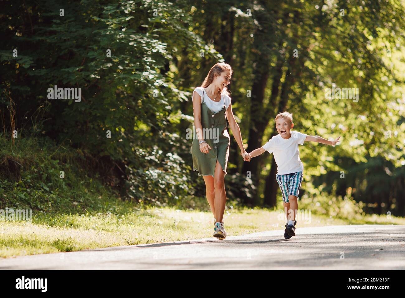 Sister teenager and little brother boy run their hands through park, sun light. Concept family sport Stock Photo