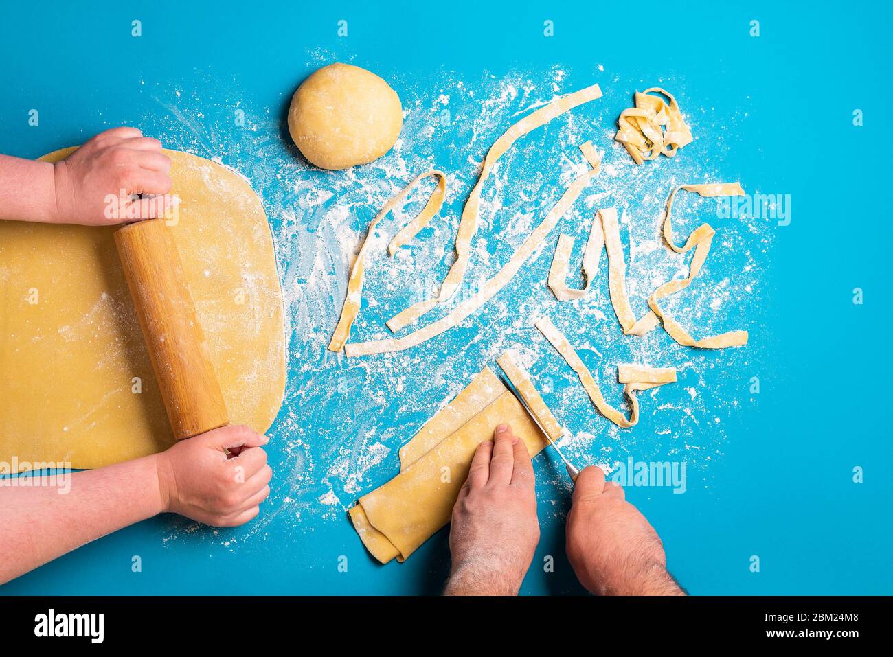 Couple preparing Italian pasta by hand on a blue background. Flat lay