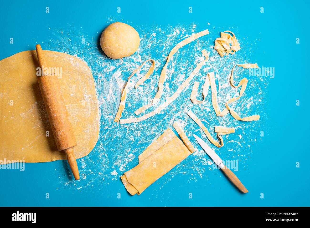Making Italian pasta at home, by hand, on a blue background. Rolling and cutting raw dough for
