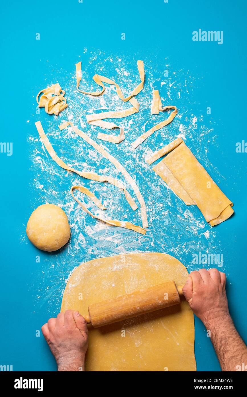 Man rolling semolina dough to make pasta, on a blue background. Top