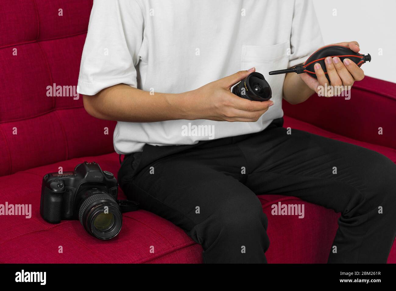 An Asian photographer is cleaning the camera and lens with a air blower