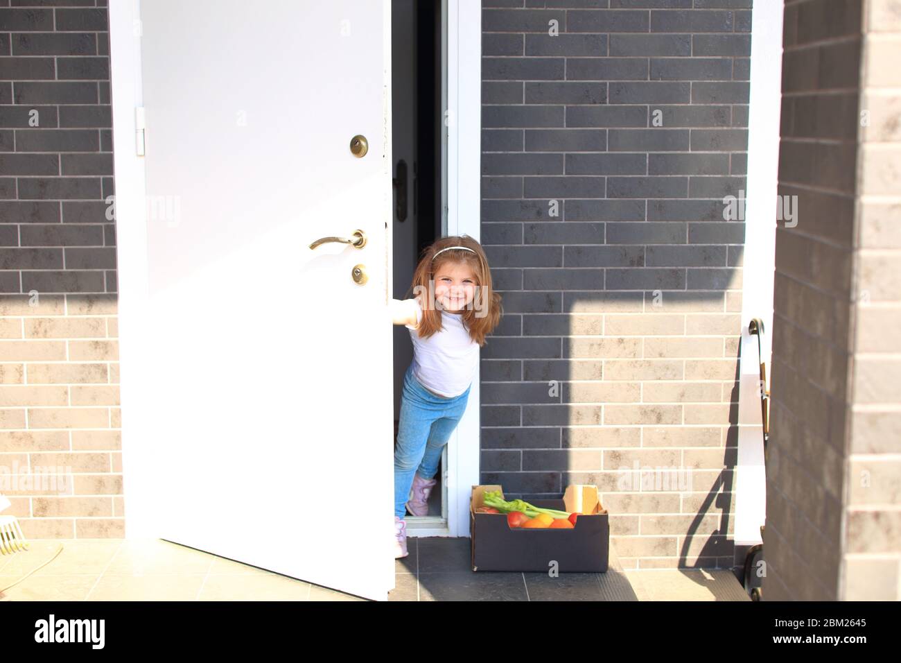Little girl peeks out from the front door. Stock Photo