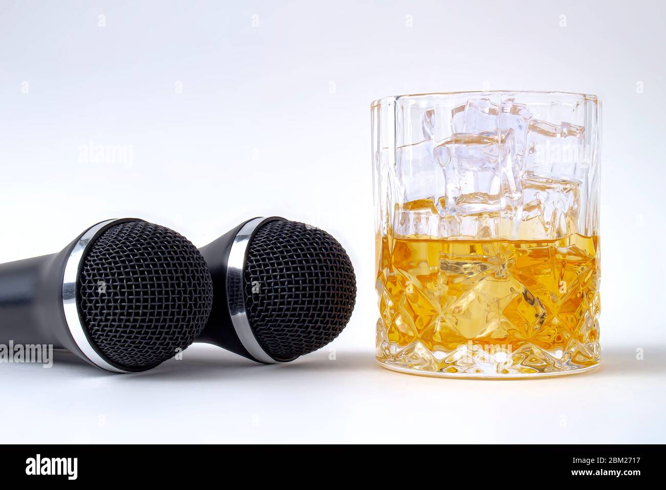 A whisky glass with ice and liquor and two karaoke microphones on a