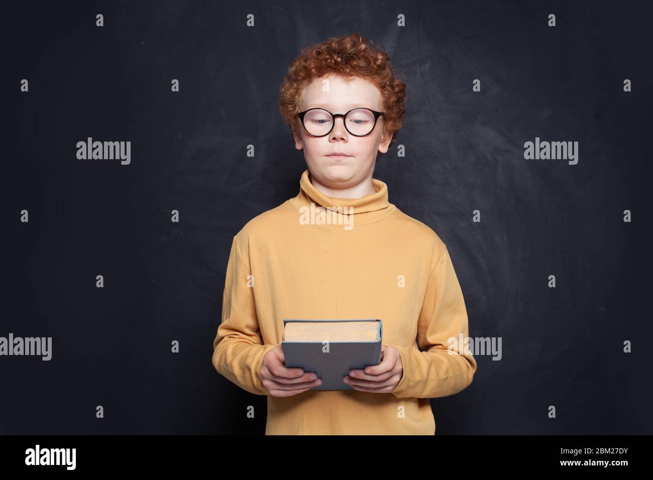 Kid looking at book on school blackboard background Stock Photo