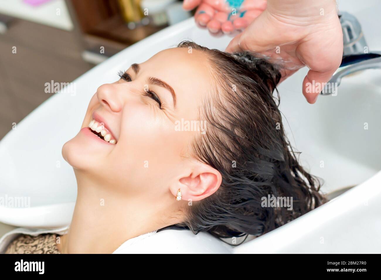 Woman is receiveng washing hair in sink laughting in hair salon Stock