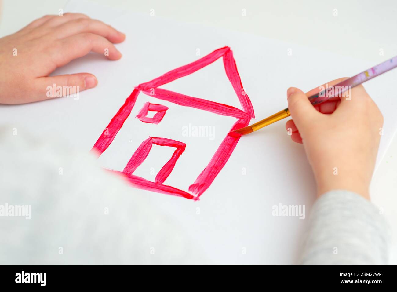 Closeup of hands of child drawing red house on white sheet of paper. Children's creativity concept. Stock Photo