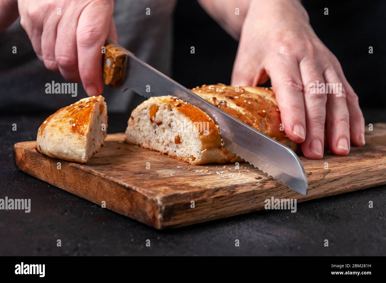 Woman Slices Homemade Wholemeal Multigrain Bread with Flax Seeds and Sesame on Wooden Board on Dark Table Stock Photo