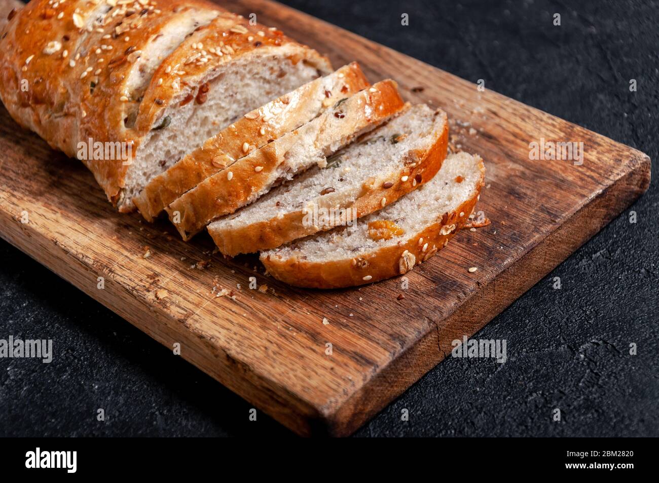 Homemade Sliced Wholemeal Multigrain Bread with Flax Seeds and Sesame on Wooden Board on Dark Table Stock Photo