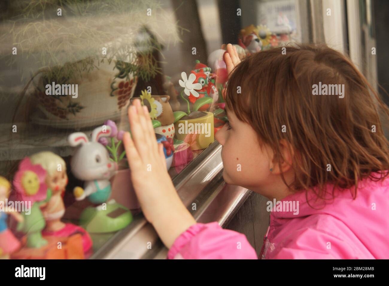 Young girl looking thought he window of a store to a solar powered small toys display Stock Photo