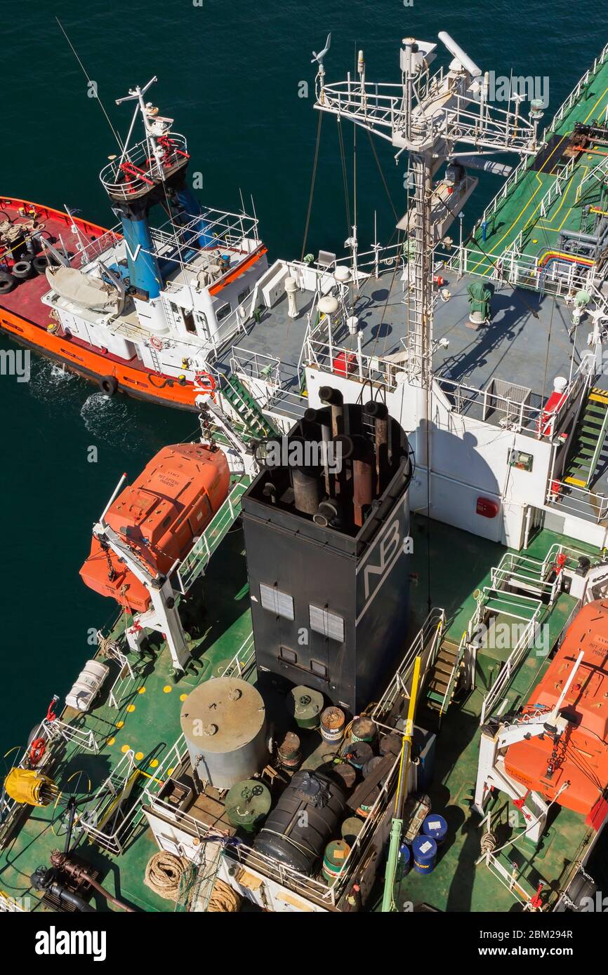 Top view of orange, red and white Nikolaos V tugboat and oil drums