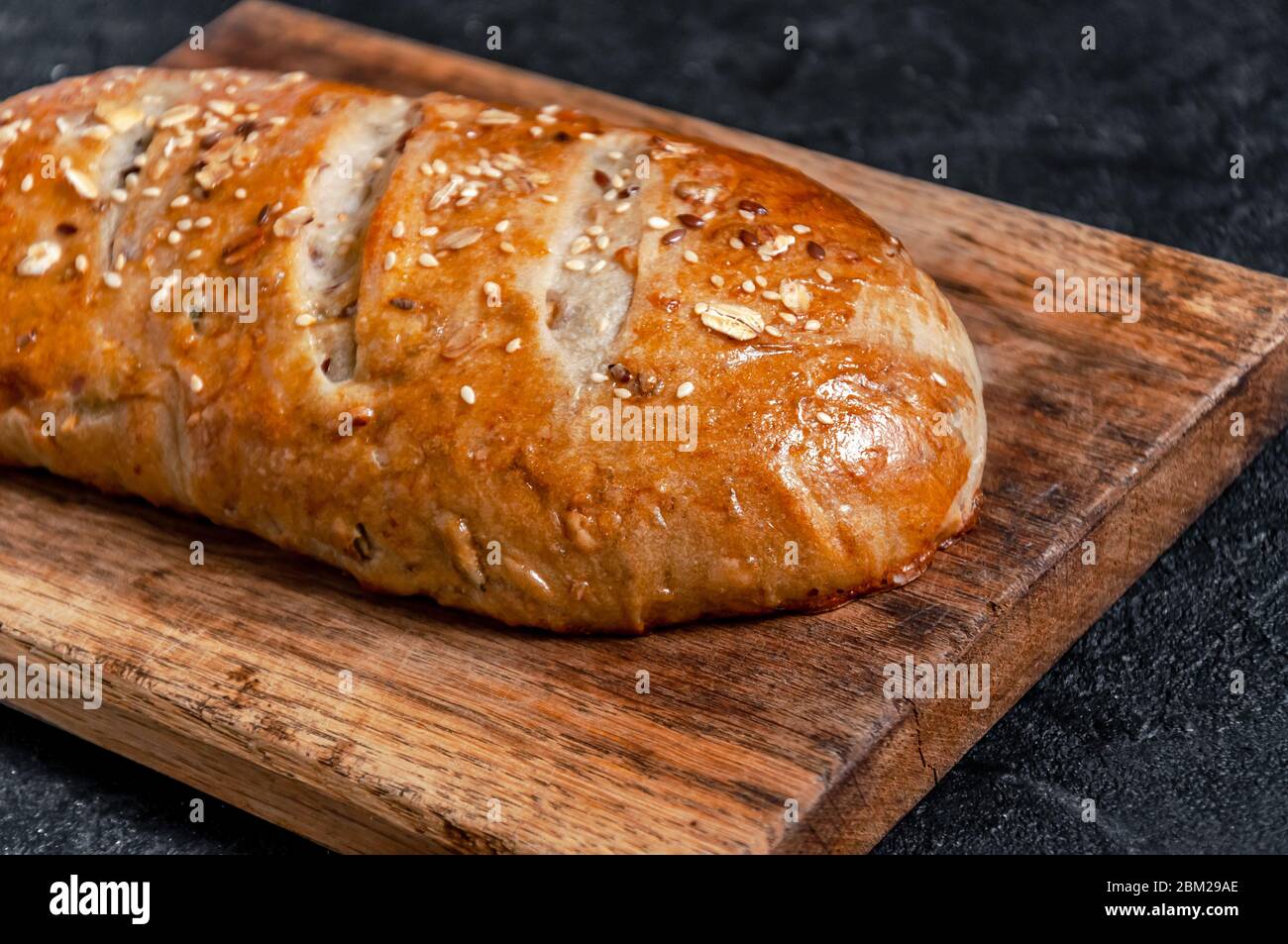 Homemade Wholemeal Multigrain Bread with Flax Seeds and Sesame on Woode Board on Dark Table. Close up Stock Photo