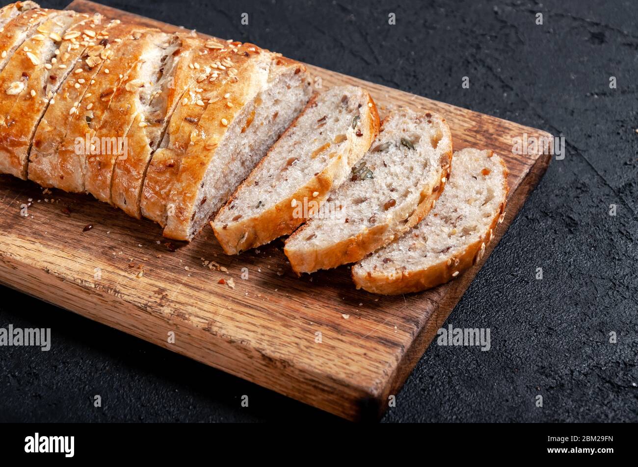 Homemade Sliced Wholemeal Multigrain Bread with Flax Seeds and Sesame on Wooden Board on Dark Table Stock Photo
