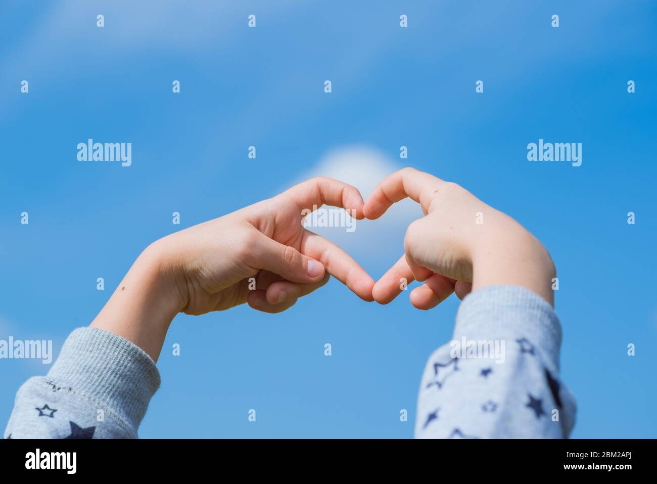 love Concept, Heart-shape hand gesture.Little girl made a heart with her  fingers against the blue sky Stock Photo - Alamy
