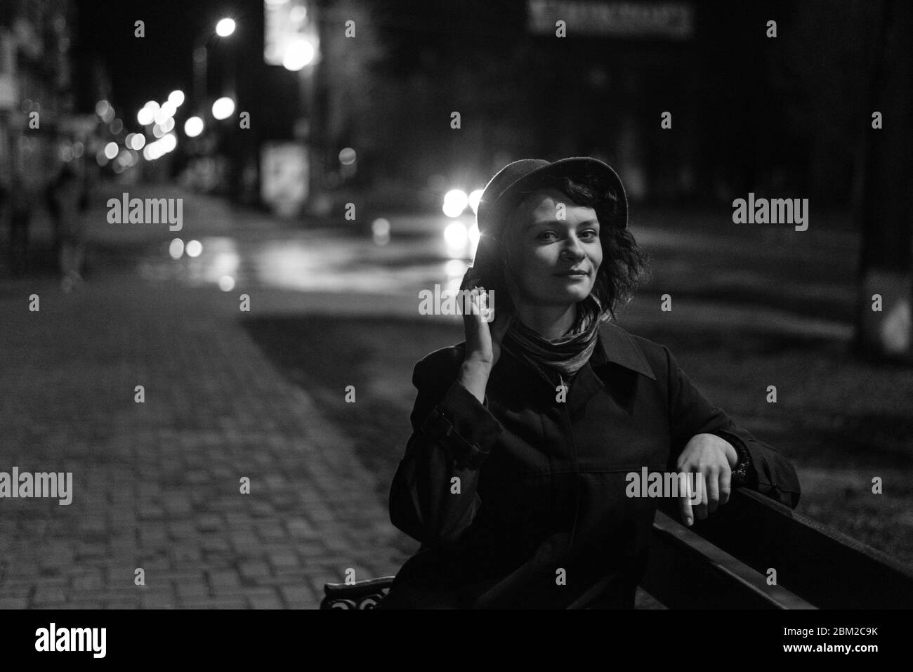 Cute girl in a hat sits on a bench on the street at night, photographed ...