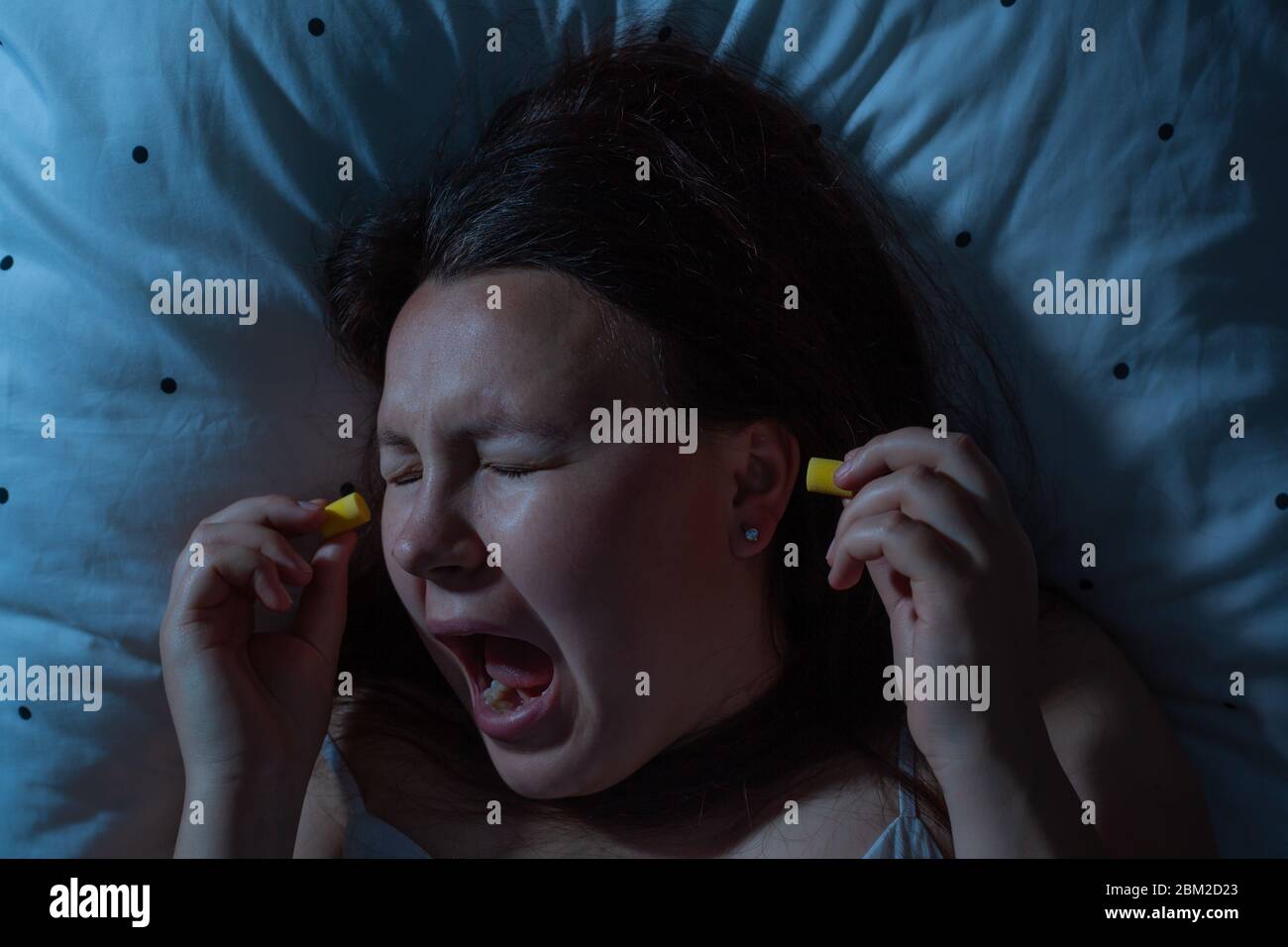 Young woman putting earplugs into her ears for the noise reduction before sleep, insomnia Stock Photo