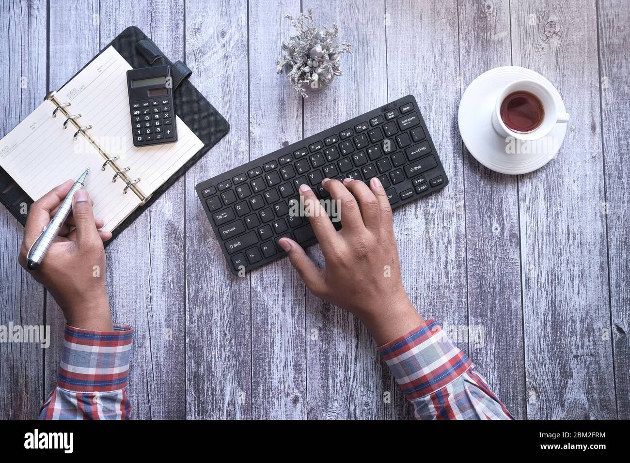 young man typing on keyboard while writing on notebook  Stock Photo