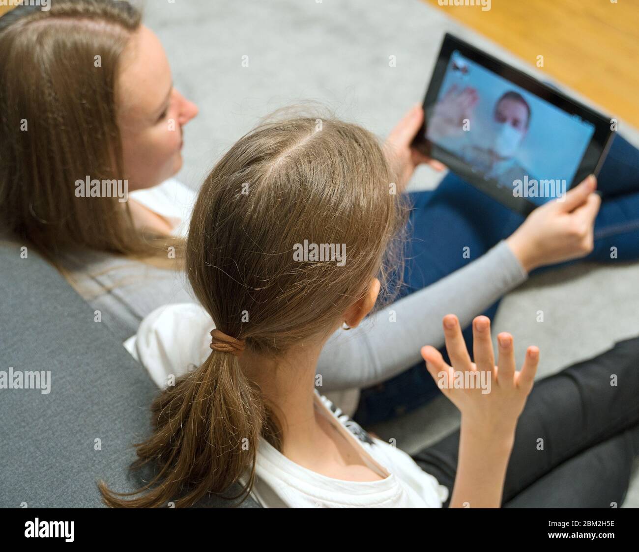 Woman and her daughter communicate with dad, who is in quarantine. Stock Photo