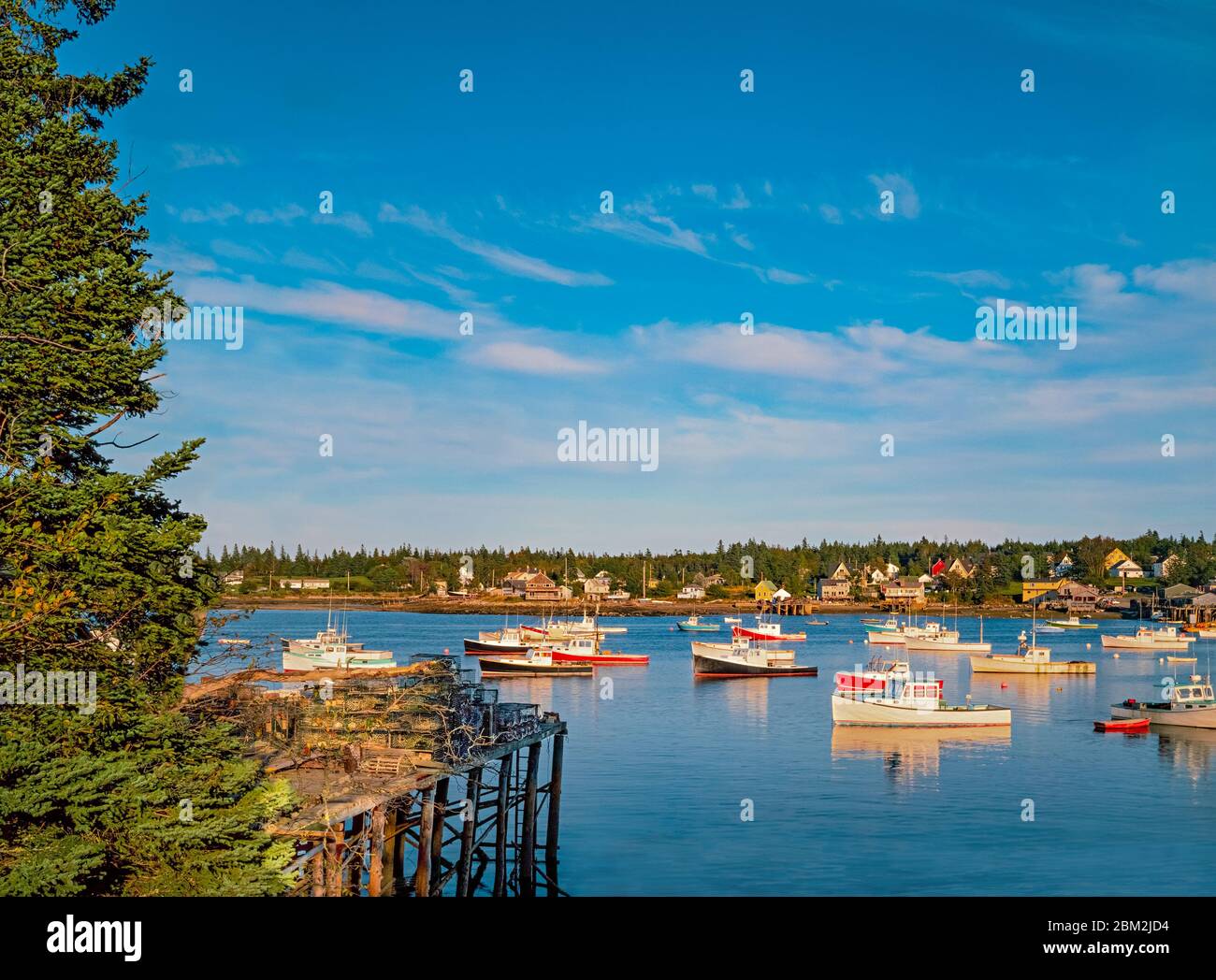 Lobster baskets sit high on a wharf at low tide in front of fishing boats in Bass Harbor, Maine. Stock Photo