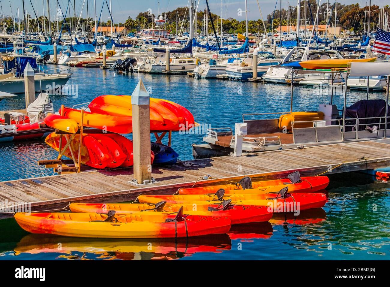 Red and yellow kayaks sit on dock in a Mission Bay marina filled with boats.  Mission Bay was created from a marsh land and is now filled with marinas Stock Photo
