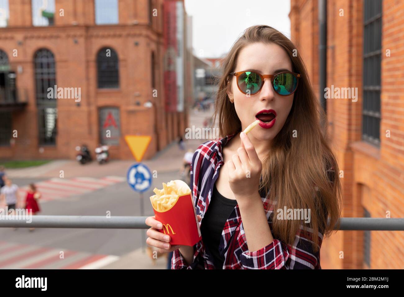 LODZ, POLAND - AUGUST 17, 2019: young girl eats french fries from a chain of McDonald's restaurants. The girl is having fun posing with her food. Stock Photo