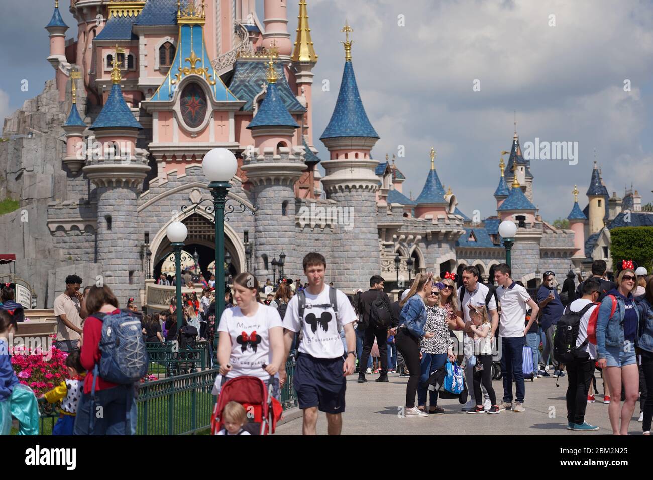 Standing on a street of a theme park in middle of a crowd of people. Walking visitors in theme park in front of a cute castle with cloudy sky. Paris F Stock Photo