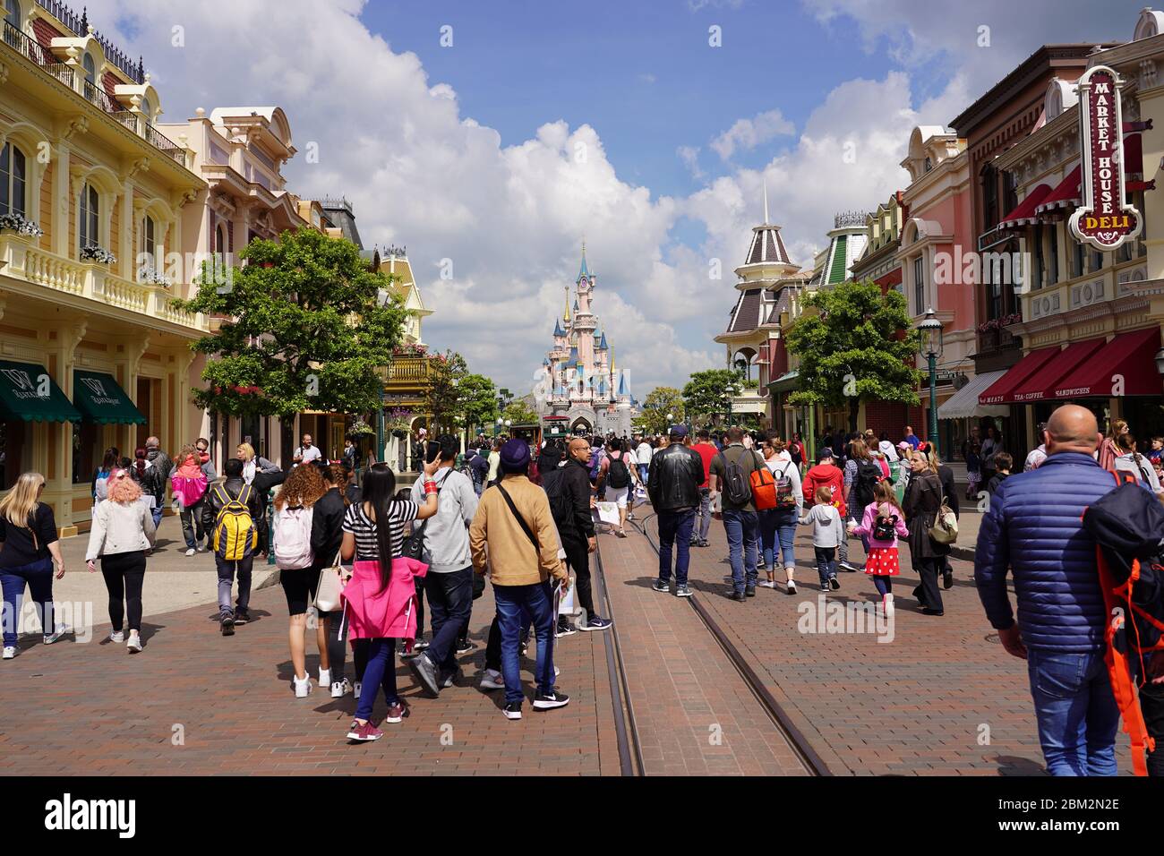 Standing on a street of a theme park in middle of a crowd of people. Walking visitors in theme park in front of a cute castle with cityscape. Paris Fr Stock Photo