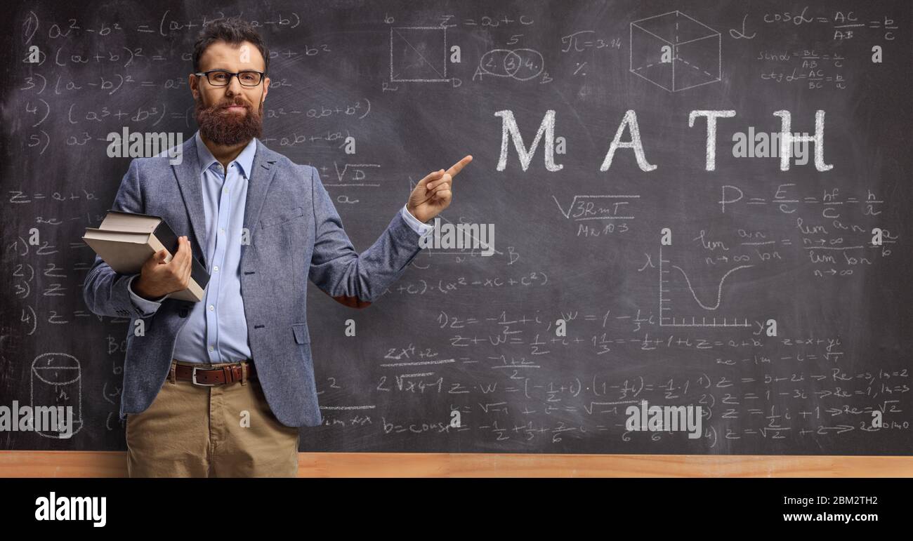 Math teacher holding books and pointing at a blackboard with formulas Stock Photo