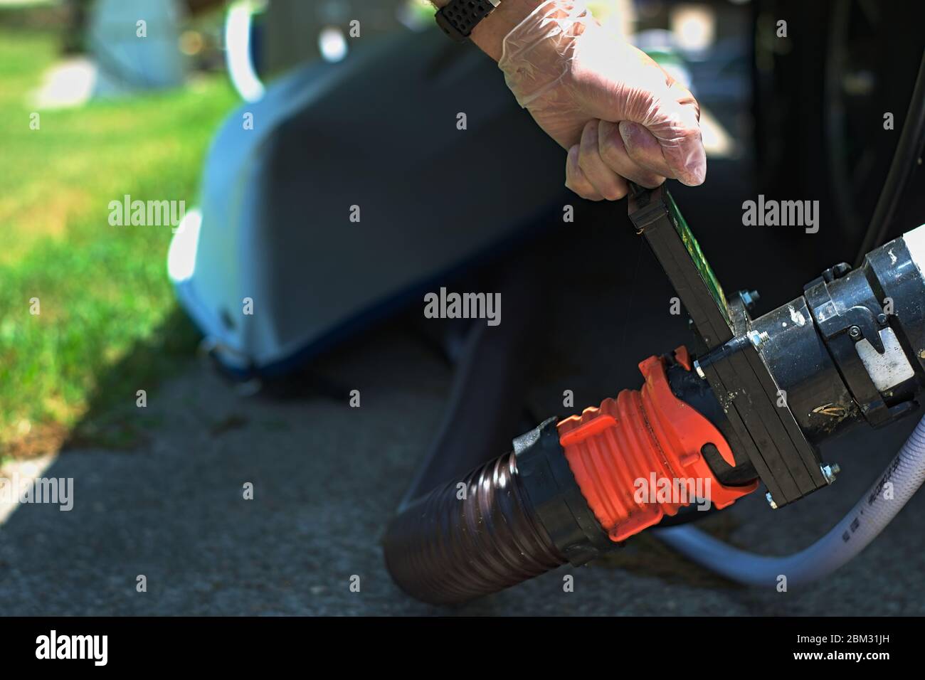 Hand dumping rv tank valve to release grey gray black waste water and sewage while parked at campsite dump station. Kayak lays in background. Stock Photo