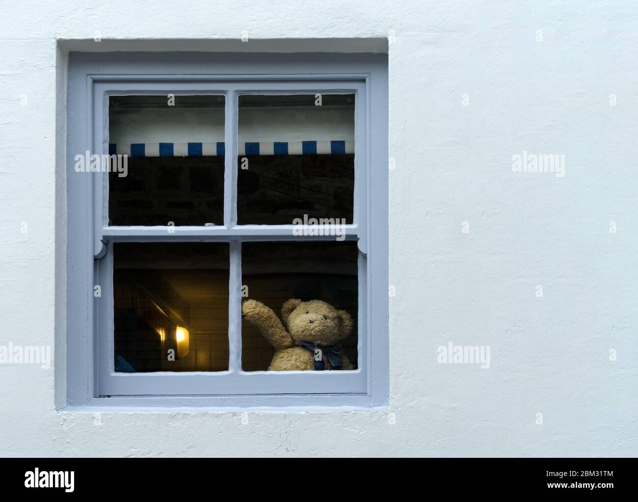 Cute teddy bear waving hello or goodbye from house window suggesting self isolation or social distancing during corona virus covid19 pandemic Stock Photo
