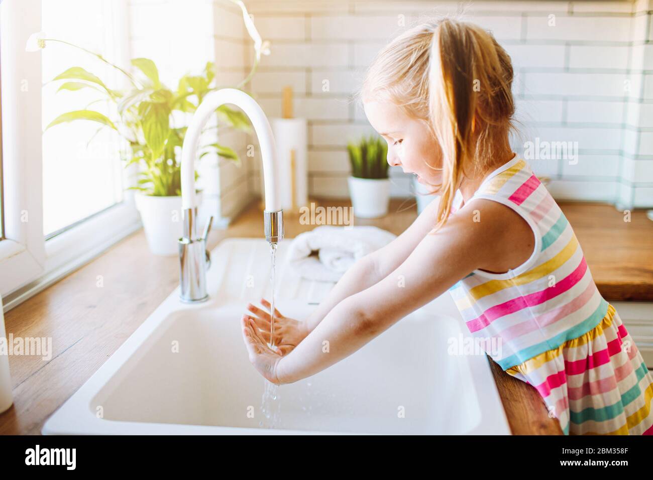 Blonde toddler girl washing hands in the lingh kitchen before eating. Hygiene and healthcare concept Stock Photo