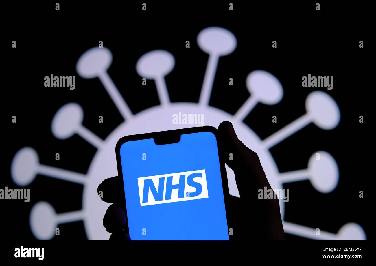 NHS app login screen on a smartphone silhouette hold in a hand and coronavirus COVID-19 image on the blurred background. Stock Photo