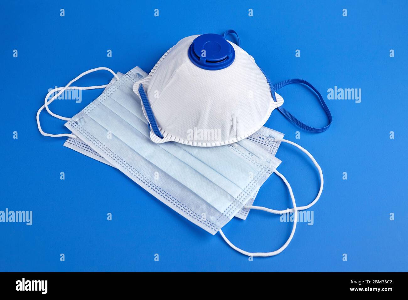 Disposable surgical face masks and white respirator on blue background. Protection against the