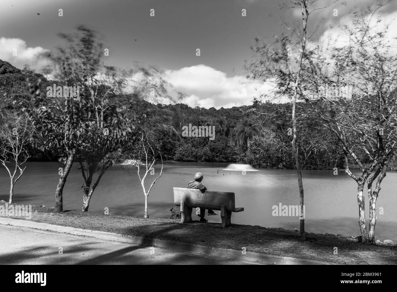 A thougtful woman seat down in a bench facing a lake in a cold day Stock Photo