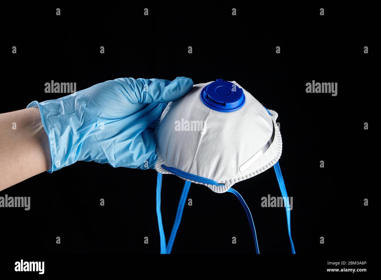 Filtering facepiece respirator in hand in blue glove, isolated on black background. N95 respirator. White FFP2 respirator, protection against coronovi Stock Photo