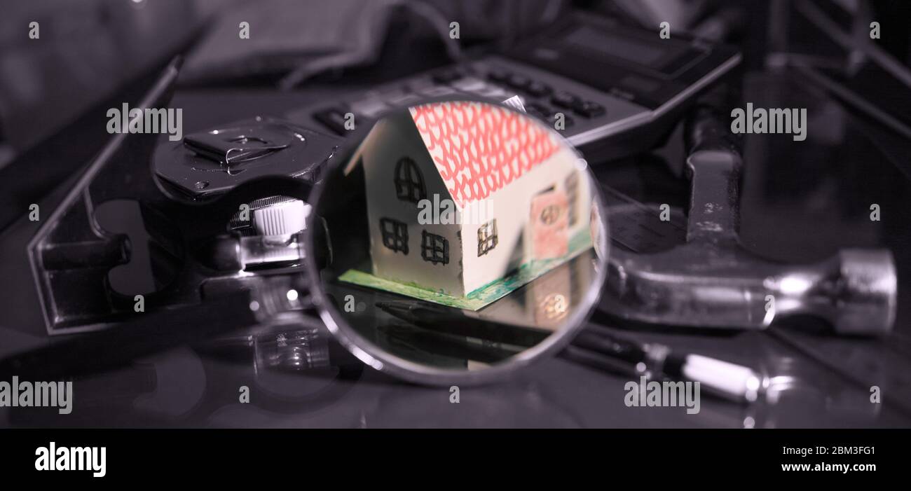 A small house seen through a magnifying glass, surrounded by tools specific to construction and home repairing... Stock Photo