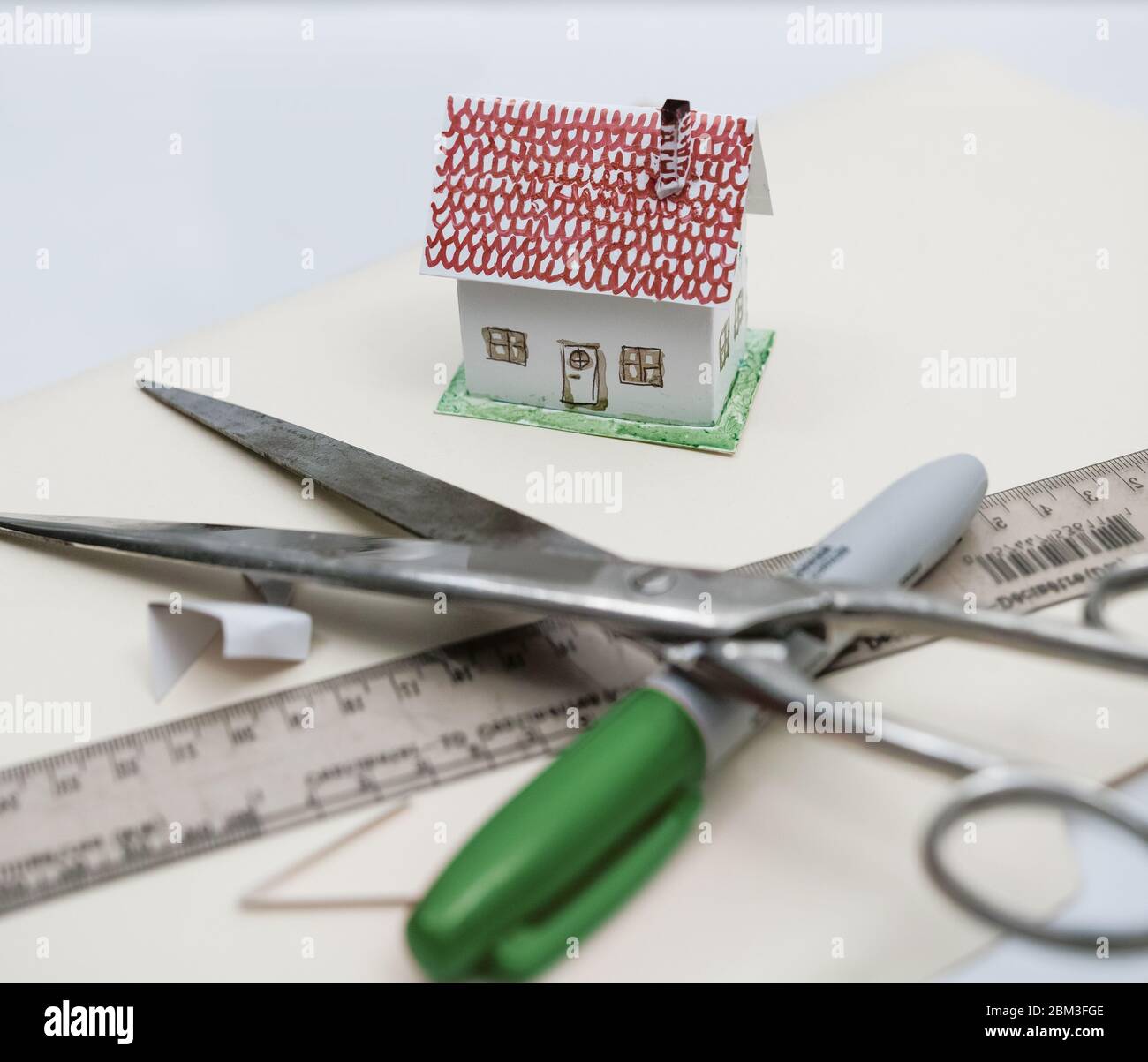A toy house built from paper and cardboard, with tools such as a marker, scissors, ruler and glue. Stock Photo