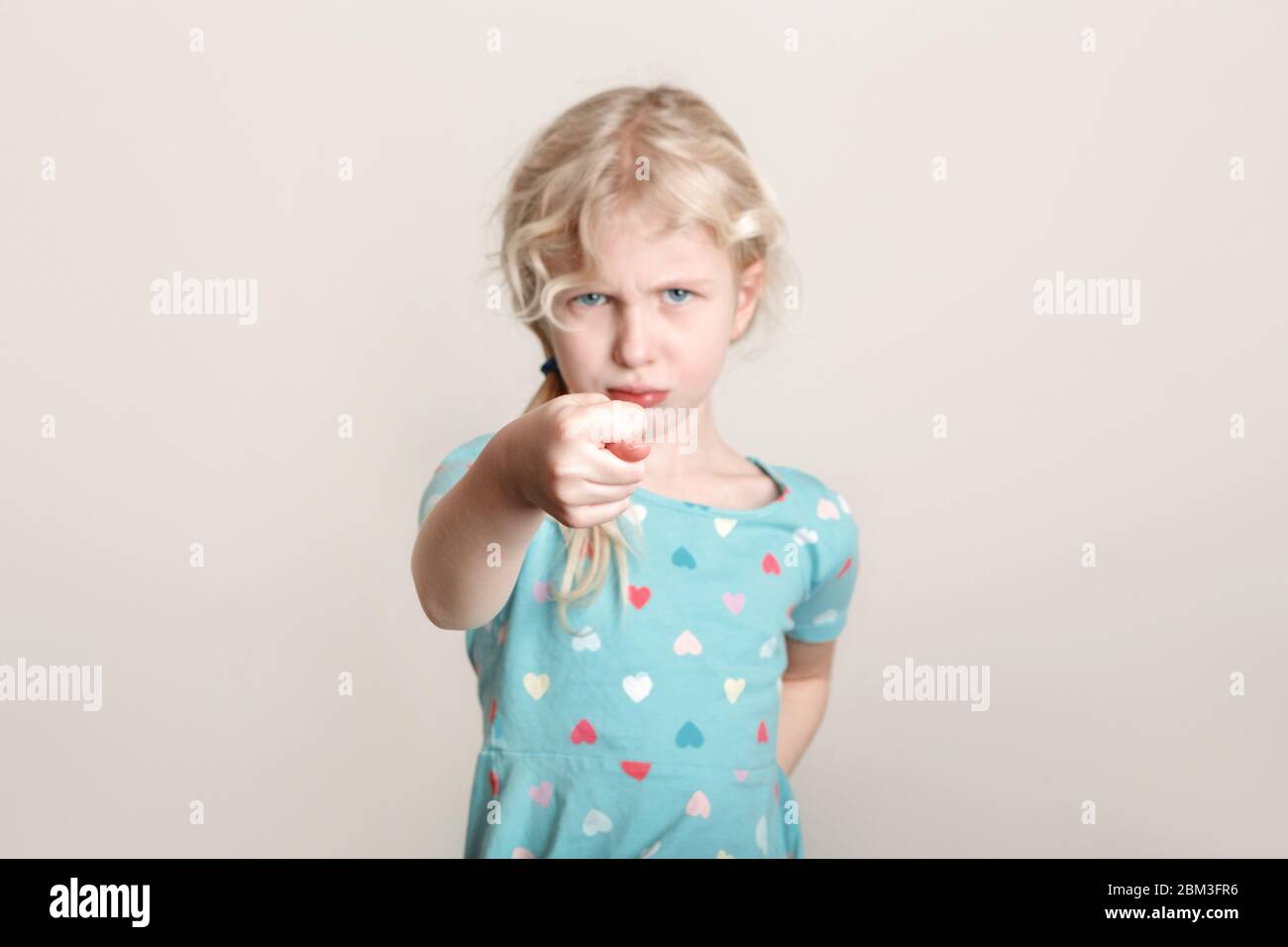 Child girl showing fig sign. Kid expressing strong negative emotion. Cute adorable blonde Caucasian preschool girl posing in studio Stock Photo