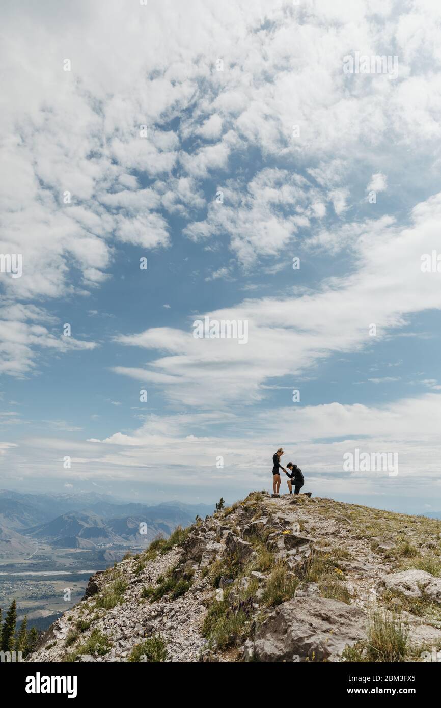 man gets on one knee to propose to his girlfriend on wyoming mountain Stock Photo